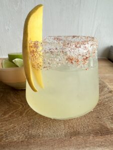 A glass of mango margarita with a salted rim and a slice of mango